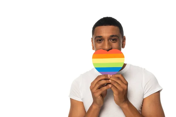 African american man covering mouth with rainbow colors paper heart isolated on white, lgbt concept — Stock Photo