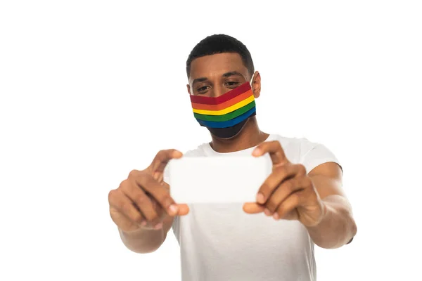 Афроамериканський чоловік в масці безпеки в кольорах lgbt і приймає селфі на смартфон ізольовано на білому — стокове фото