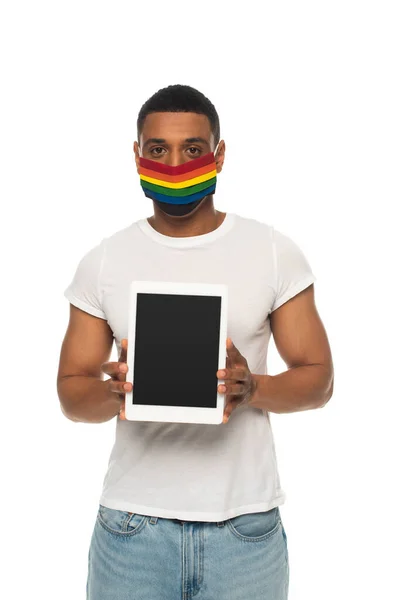 Uomo afroamericano indossando colori lgbt maschera medica e mostrando tablet digitale con schermo bianco isolato su bianco — Foto stock