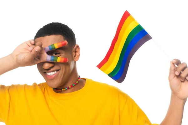 Fröhlicher afrikanisch-amerikanischer Mann zeigt Siegesgeste, während er die lgbt-Fahne isoliert auf weiß hält — Stockfoto