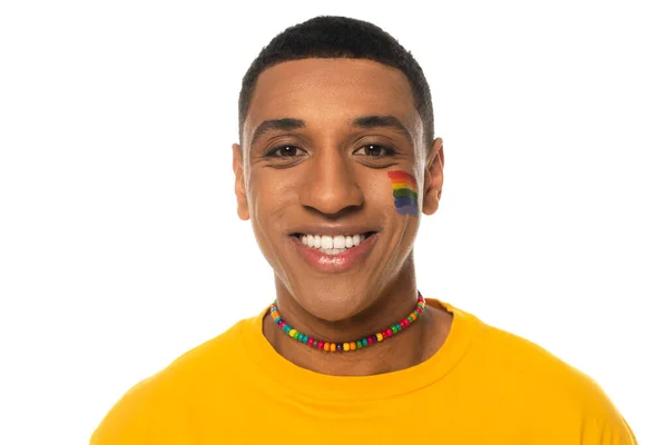 Hombre afroamericano con bandera lgbt pintado en la cara sonriendo a la cámara aislado en blanco - foto de stock