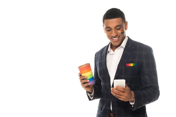 African american businessman with lgbt flag painted on face holding coffee to go and smartphone isolated on white — Stock Photo
