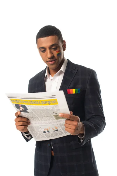 African american businessman with lgbt flag painted on face reading newspaper isolated on white — Stock Photo