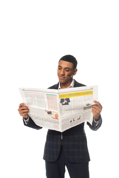 Positive african american businessman with lgbt flag painted on face reading newspaper isolated on white — Stock Photo