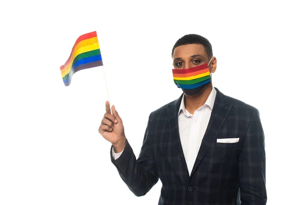 Homme d'affaires afro-américain portant un masque médical aux couleurs arc-en-ciel et tenant le drapeau lgbt isolé sur blanc — Photo de stock