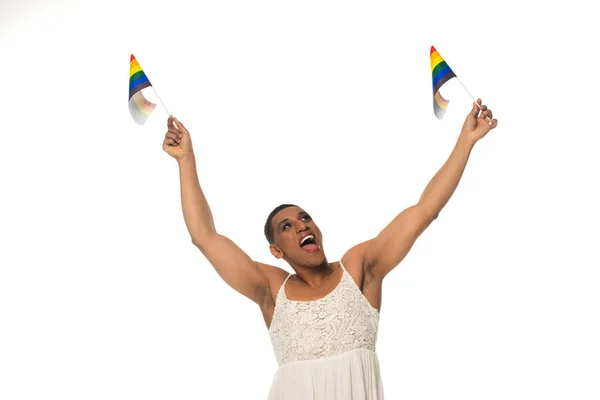 Excité afro-américain transgenre homme en robe de soleil tenant lgbt drapeaux dans les mains levées isolé sur blanc — Photo de stock