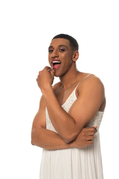 Africano americano transexual hombre mirando cámara mientras aplicando lápiz labial aislado en blanco - foto de stock