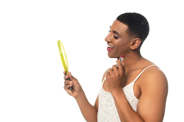 Africano americano transexual hombre sonriendo mientras celebración de lápiz labial y espejo aislado en blanco - foto de stock