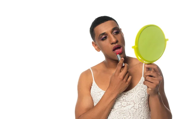 Africano americano transgénero hombre en vestido de sol celebración espejo y la aplicación de lápiz labial aislado en blanco - foto de stock