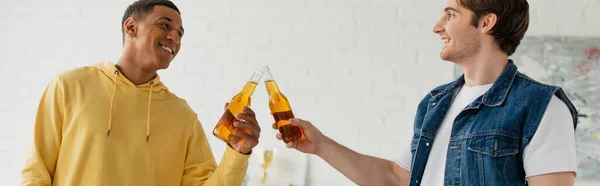 Junge lächelnde interrassische Freunde klirren mit Bierflaschen, Transparent — Stockfoto