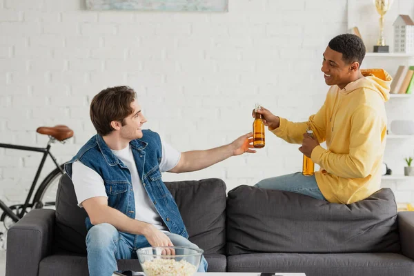 Positive young interracial friends drinking beer together in living room — Stock Photo