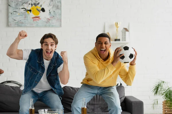 Animado interracial futebol fãs assistindo jogo e celebrando triunfo na moderna sala de estar — Fotografia de Stock