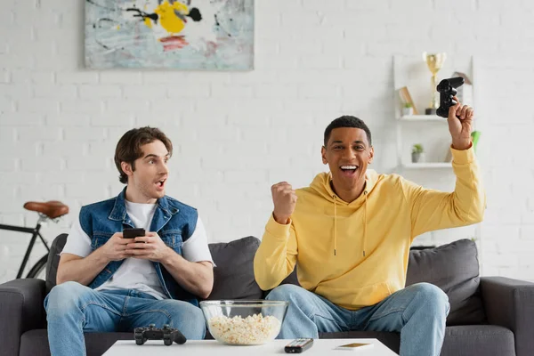 KYIV, UKRAINE - MARCH 22, 2021: excited interracial friends celebrating victory in video game — Stock Photo