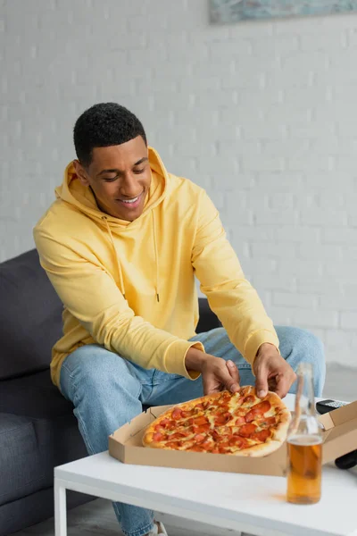 Hipster africano americano comendo pizza perto de garrafa com cerveja em casa — Fotografia de Stock