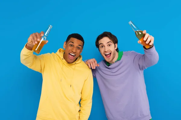 Fröhliche interrassische Freunde lough und feiern mit Flaschen Bier isoliert auf blau — Stockfoto
