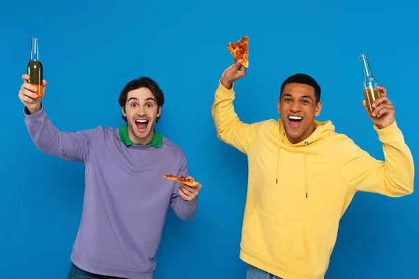 Interracial friends enjoying pizza with beer isolated on blue — Stock Photo