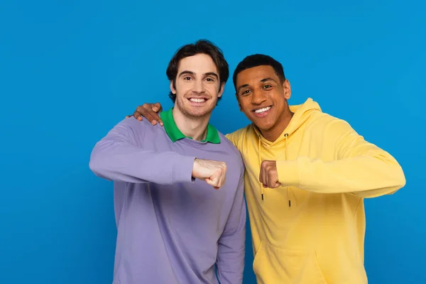Abbracciare hipster interrazziale sorridente con pugno gesto urto isolato su blu — Foto stock