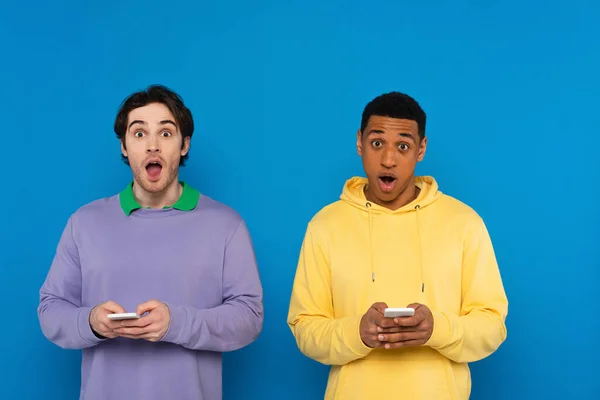 Interracial friends with smartphones in hands isolated on blue — Stock Photo