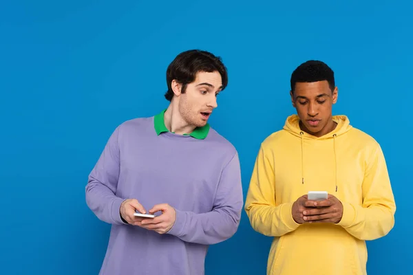 Curious hipster peeking at smartphone of african american man friend isolated on blue — Stock Photo