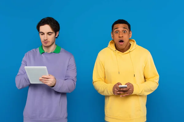 Interracial hipsters holding gadgets in hands isolated on blue — Stock Photo
