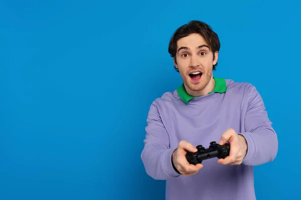 QUIIV, UCRÂNIA - MARÇO 22, 2021: jovem segurando joystick e olhando para a câmera isolada em azul — Fotografia de Stock