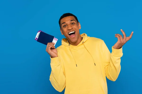 Feliz homem afro-americano segurando passaporte com passagens aéreas em mãos isoladas em azul — Fotografia de Stock