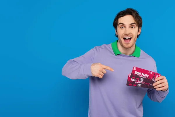 Sonriente joven mostrando entradas de concierto con el dedo gesto aislado en azul - foto de stock