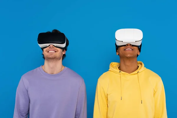 Hipsters inter-raciais em fones de ouvido de realidade virtual isolados em azul — Fotografia de Stock