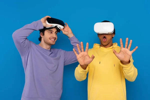 Interracial hipsters playing game with virtual reality headsets isolated on blue — Stock Photo