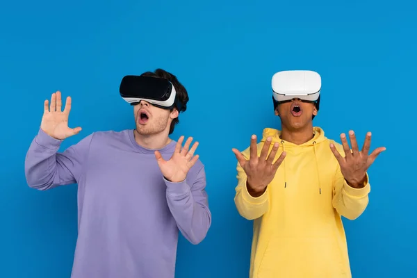 Interracial hipsters playing simulation game with virtual reality headsets isolated on blue — Stock Photo