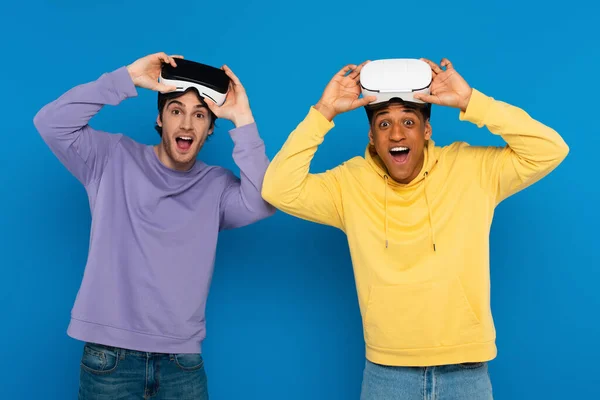 Excited interracial hipsters with virtual reality headsets on heads isolated on blue — Stock Photo