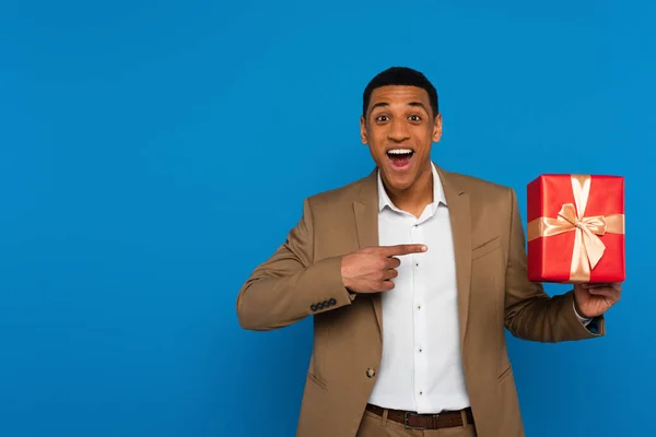 Jovem animado afro-americano homem apontando com dedo para caixa de presente isolado em azul — Fotografia de Stock