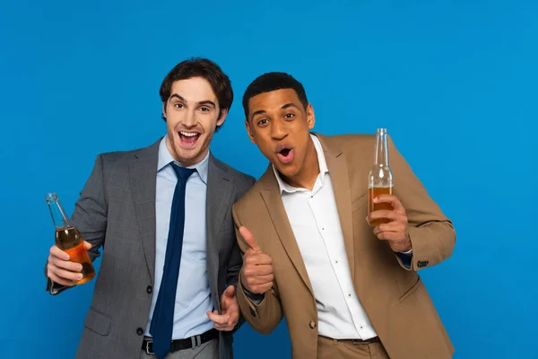 Amigos inter-raciais em ternos celebrando o sucesso com garrafas de cerveja e polegares até gestos isolados em azul, banner — Fotografia de Stock