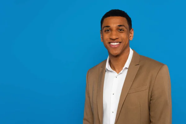 Sonriente hombre afroamericano en elegante chaqueta mirando a la cámara aislada en azul - foto de stock