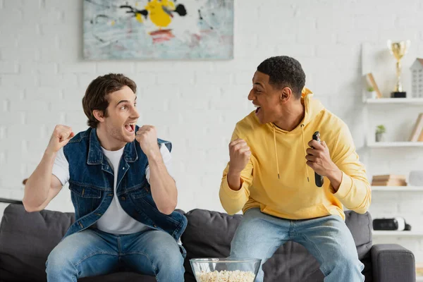 Excited interracial friends watch tv and eating popcorn in modern loft — Stock Photo