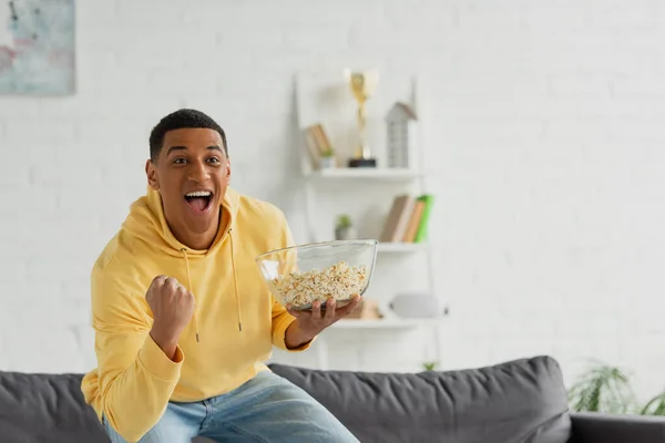 Animado afro-americano homem assistindo tv com pipocas no loft moderno — Fotografia de Stock