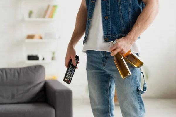 Cropped view of man with beer bottles and tv remote controller in hands on blurred background — Stock Photo