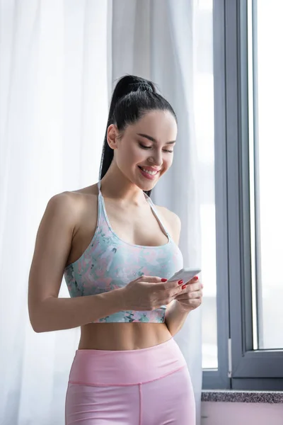 Felice donna sportiva chatta su smartphone vicino alla finestra di casa — Foto stock