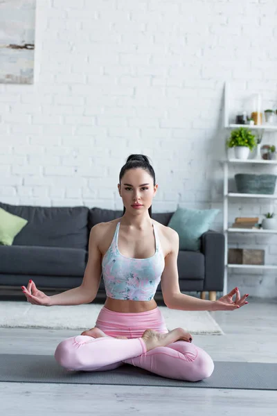 Hübsche barfüßige Frau schaut in die Kamera, während sie in Lotus-Pose meditiert — Stockfoto