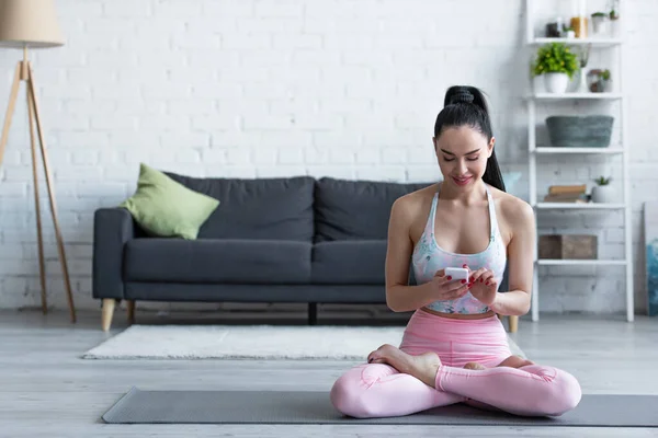 Ziemlich sportliche Frau plaudert auf Handy, während sie in Lotus-Pose sitzt — Stockfoto