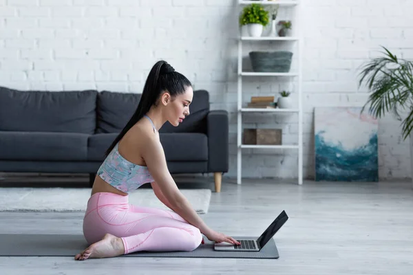 Vista lateral da mulher descalça usando laptop enquanto sentado no tapete de ioga — Fotografia de Stock