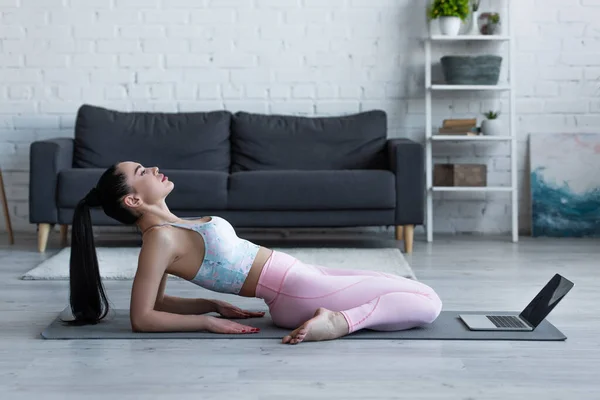 Seitenansicht einer praktizierenden Heldin posiert auf Yogamatte in Laptopnähe — Stock Photo