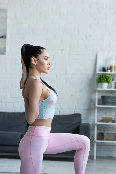 Vista lateral de la mujer bonita haciendo ejercicio de estiramiento con las manos detrás de la espalda - foto de stock