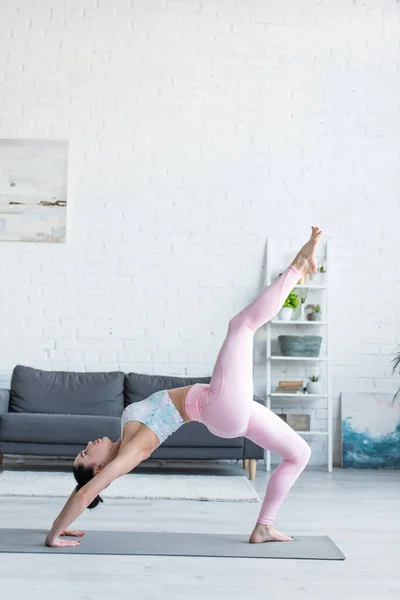 Side view of young woman in sportswear practicing yoga in one legged wheel pose — Stock Photo