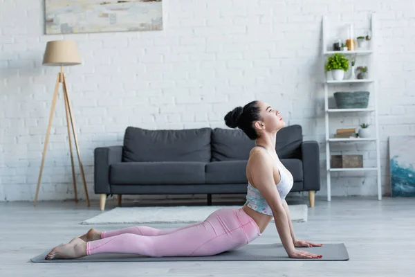 Vue latérale de la jeune femme brune pratiquant le yoga en pose de cobra élevé — Photo de stock