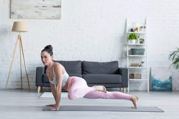 Junge Frau in Sportkleidung übt zu Hause in einbeiniger Plankenpose — Stockfoto