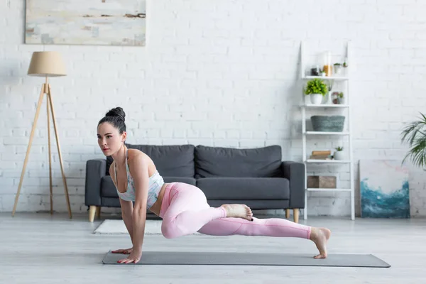 Jovem mulher em sportswear praticando em uma postura de prancha de perna em casa — Fotografia de Stock