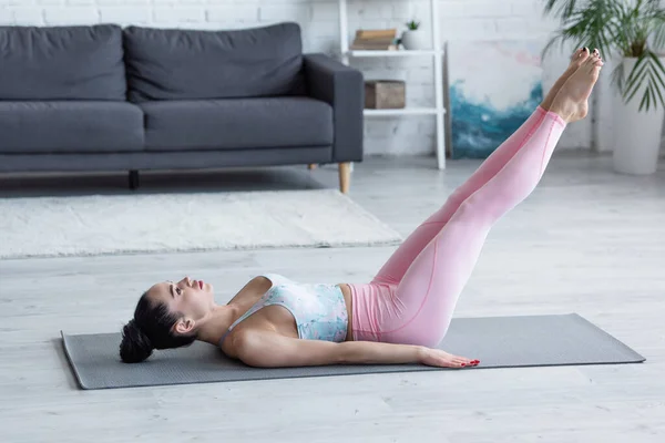 Joven mujer en ropa deportiva practicando rejuvenecimiento pose en esterilla de yoga - foto de stock