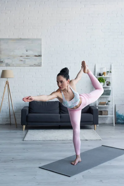 Morena mujer de pie en el señor de la pose de baile mientras practica yoga en casa - foto de stock