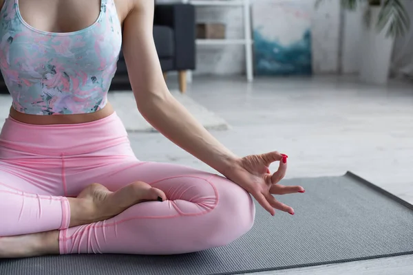 Vista recortada de mujer descalza en ropa deportiva meditando en pose de loto - foto de stock